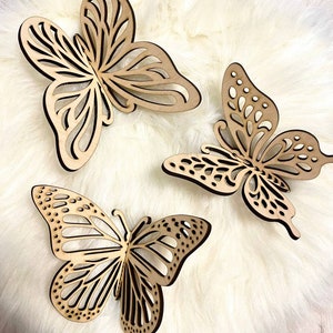 May include: Three wooden butterfly wall decor pieces in a light brown color. The butterflies are intricately cut with a delicate design and have a natural wood finish.