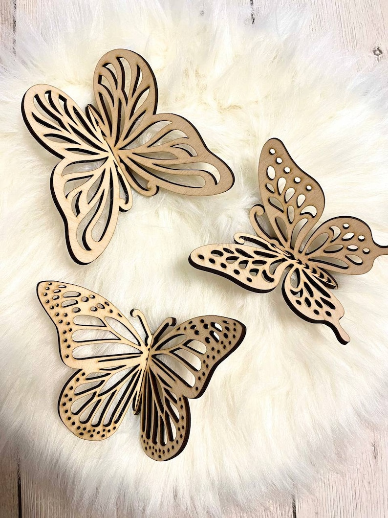 May include: Three wooden butterfly wall decor pieces in a light brown color. The butterflies are intricately cut with a delicate design and have a natural wood finish.