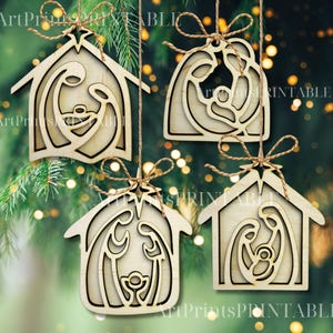 May include: Four wooden Christmas ornaments with a nativity scene design. Each ornament is a different shape, with a natural wood finish and a twine hanger. The ornaments are hanging against a blurred green background with bokeh lights.