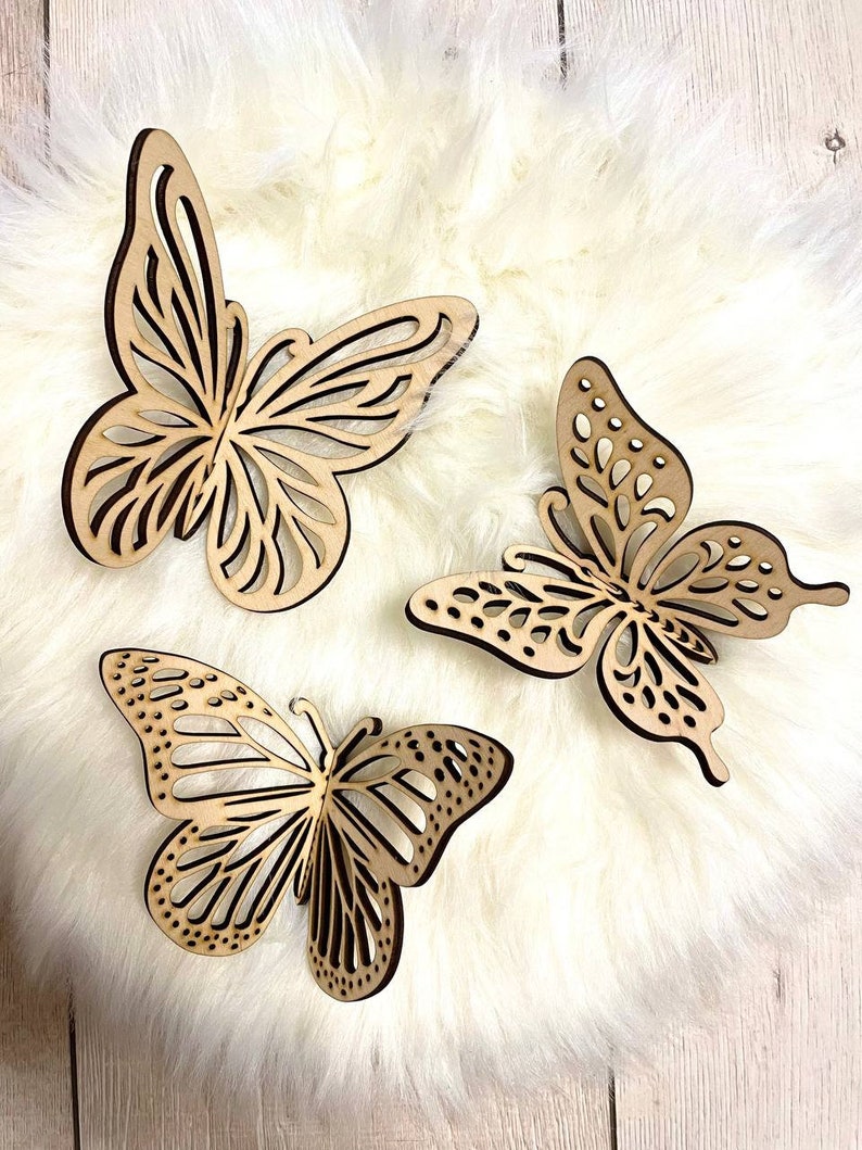 May include: Three wooden butterfly wall decor pieces in a light brown color. The butterflies are intricately cut with a delicate design and have a natural wood finish.