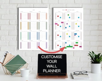 May include: Two wall calendars for 2026, one blank and one with color-coded notes, hang above a desk. A laptop displays "CUSTOMISE YOUR WALL PLANNER." A gold wire basket holds books and a mug. A potted plant and glasses complete the scene.