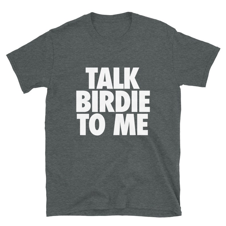 May include: Dark heather gray t-shirt with the text "TALK BIRDIE TO ME" in bold white letters. The shirt has short sleeves and a crew neck. A casual tee for everyday wear.