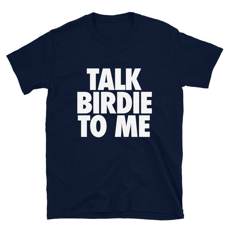 May include: Navy blue t-shirt with the white text "TALK BIRDIE TO ME" in a bold, sans-serif font. The shirt is a short-sleeved crew neck, likely made of cotton or a similar fabric. The text is centered on the chest.