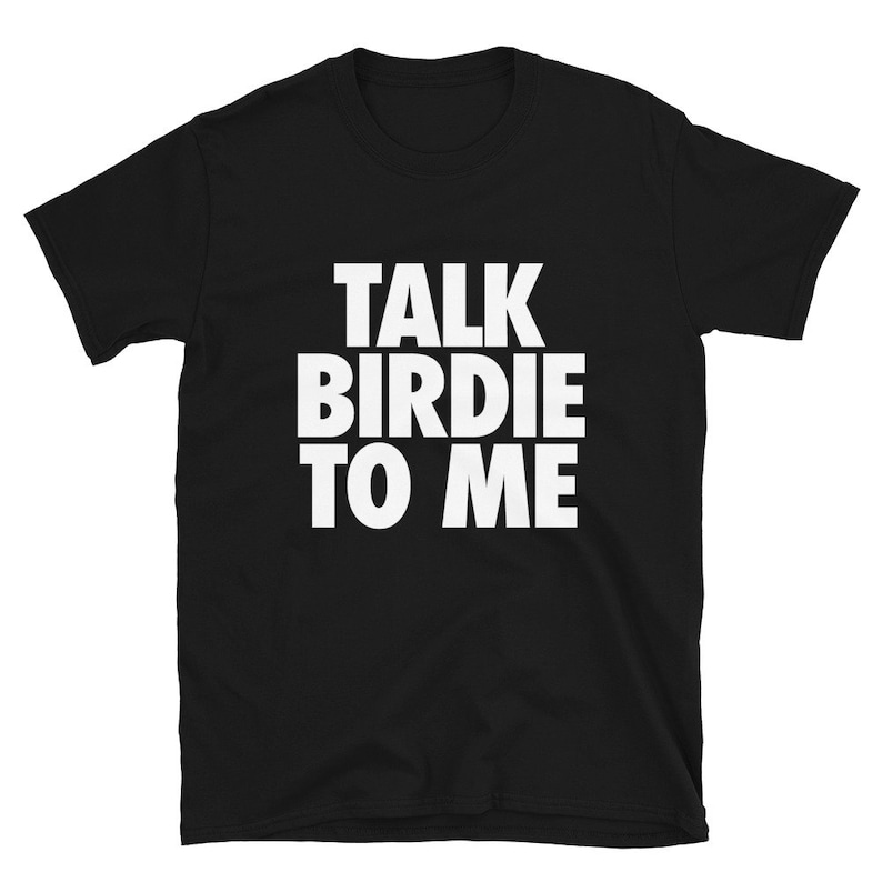 May include: Black t-shirt with the white text "TALK BIRDIE TO ME" in a bold, sans-serif font. The shirt is made of a soft material and has short sleeves and a crew neck. The text is centered on the front of the shirt.