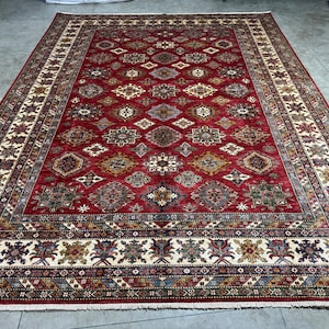 May include: A red, cream, and blue patterned rug with a geometric design. The rug has a fringe border.