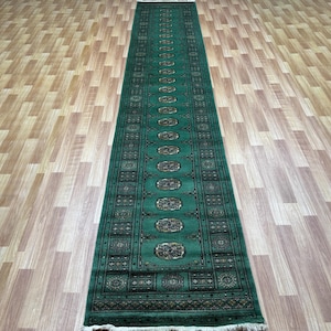 May include: A green runner rug with a traditional Persian design. The rug has a dark green border with intricate patterns and a light green centre with a repeating oval pattern.