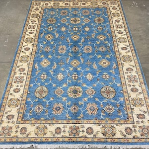 May include: A blue rug with a cream-coloured border and intricate floral patterns. The rug has a fringed edge.