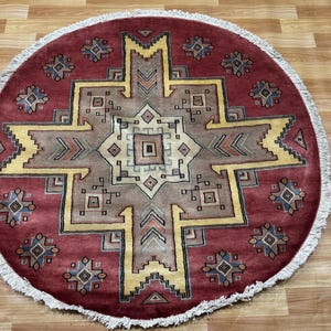 May include: A round red rug with a geometric pattern in shades of yellow, brown, and blue. The rug has a fringe border.