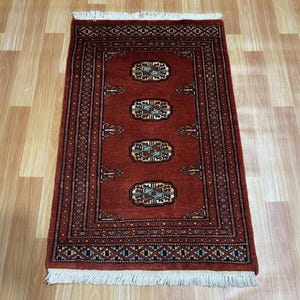 May include: A red runner rug with a traditional Persian design. The rug has a white fringe on both ends and features a repeating pattern of intricate floral motifs.