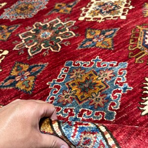 May include: A red rug with a detailed pattern of blue, yellow, and green geometric shapes. The rug has a fringe border.