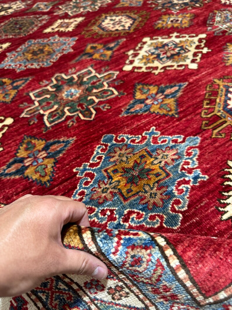 May include: A red rug with a detailed pattern of blue, yellow, and green geometric shapes. The rug has a fringe border.