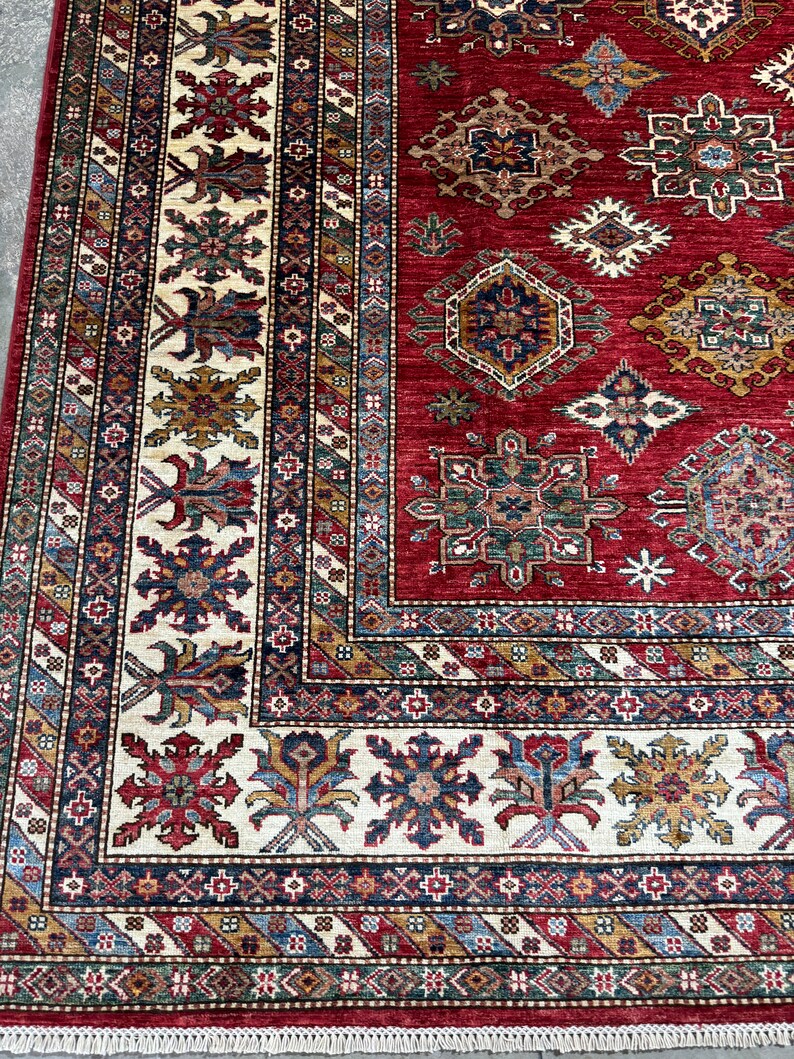 May include: A red, blue, and cream colored rug with intricate geometric patterns. The rug has a fringe border.