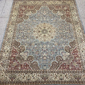 Puede incluir: Una alfombra persa tradicional con un esquema de color azul, beige y rojo. La alfombra presenta un medallón central con intrincados patrones florales y un borde con motivos repetidos.