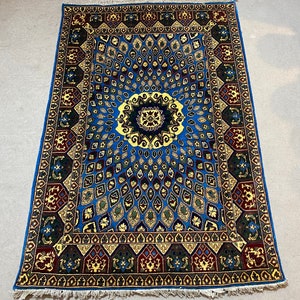 May include: A blue and gold rug with an intricate geometric pattern. The rug has a central medallion with a floral design. The rug is surrounded by a border with a repeating pattern.