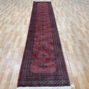 May include: A long, narrow red runner rug with a traditional Persian design. The rug has a dark brown border with intricate patterns and a central field with a repeating floral motif.