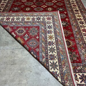 May include: A red, cream, and blue patterned rug with intricate designs. The rug is folded in half, revealing the underside of the rug.