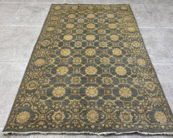 Puede incluir: Una alfombra azul oscuro con un patrón geométrico en un tono dorado más claro. La alfombra tiene un borde con flecos.