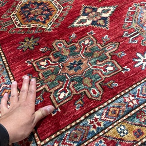 May include: A red rug with a traditional Persian design. The rug has intricate patterns in shades of blue, green, and gold. The rug is made of wool and has a soft, luxurious feel.