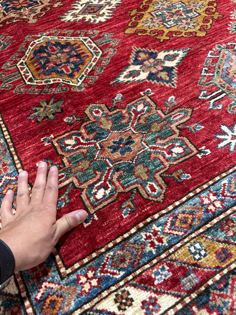 May include: A red rug with a traditional Persian design. The rug has intricate patterns in shades of blue, green, and gold. The rug is made of wool and has a soft, luxurious feel.