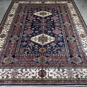 May include: A large, rectangular rug with a navy blue field and intricate geometric patterns in cream, red, and gold. The rug features a central diamond motif and a detailed border.
