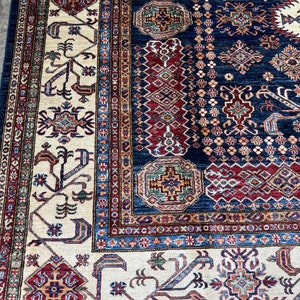 May include: A detailed close-up of a traditional rug with a navy blue background and intricate patterns. The rug features cream, red, and brown geometric designs, with a border of repeating motifs. The rug's texture and color palette create a warm, inviting feel.
