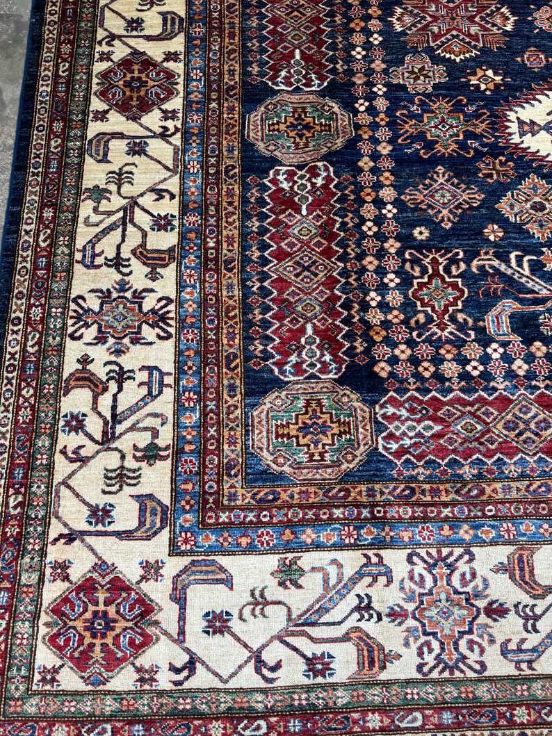 May include: A detailed close-up of a traditional rug with a navy blue background and intricate patterns. The rug features cream, red, and brown geometric designs, with a border of repeating motifs. The rug's texture and color palette create a warm, inviting feel.