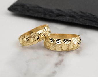 May include: Two gold rings featuring a textured nugget-style surface with alternating polished and matte facets. The bands have a continuous, irregular pattern of small, raised metallic shapes that create a reflective, multi-dimensional appearance.
