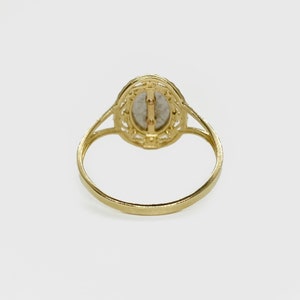 The backside of a gold ring. The back is smooth and flat, with no visible markings or engravings. The ring's band is thin and delicate, tapering slightly towards the back.
