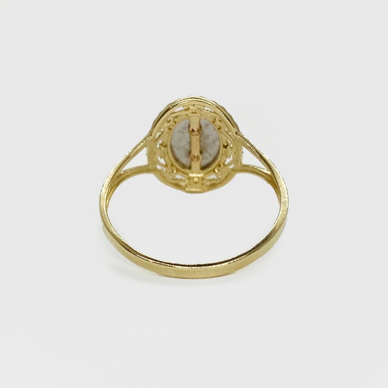 The backside of a gold ring. The back is smooth and flat, with no visible markings or engravings. The ring's band is thin and delicate, tapering slightly towards the back.