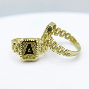 May include: Two gold rings, one with a square-shaped initial "A" and the other with a chain-link design.