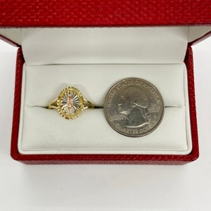 A gold ring in a red velvet box features a Virgin Mary medallion with a sunburst pattern in yellow gold. The thin, slender gold band offers an elegant, feminine look, emphasizing religious symbolism.