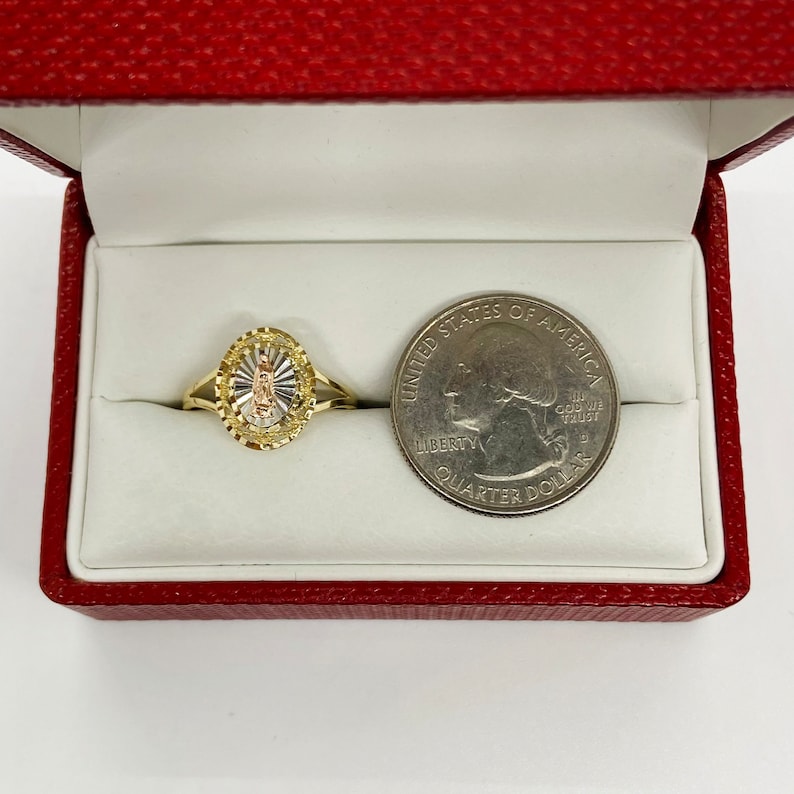A gold ring in a red velvet box features a Virgin Mary medallion with a sunburst pattern in yellow gold. The thin, slender gold band offers an elegant, feminine look, emphasizing religious symbolism.