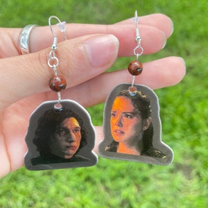 May include: A pair of silver earrings with brown beads and images of Rey and Kylo Ren from Star Wars.