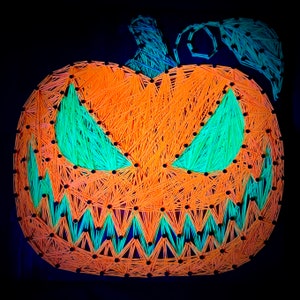 May include: A string art pumpkin with a scary face. The pumpkin is orange and the face is made of green string.