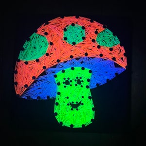 May include: A neon green mushroom with a smiling face, made with string art. The mushroom cap is red, blue, and green.