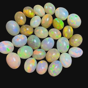May include: A selection of oval opals in shades of white, yellow, orange, and green, set against a black backdrop. The opals have a smooth, polished finish and display a vibrant play of colour.