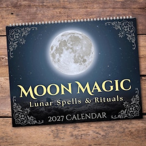 May include: A 2027 wall calendar titled Moon Magic: Lunar Spells & Rituals. The cover features a large, detailed full moon centered against a dark blue starry night sky, with decorative filigree corners and a spiral binding at the top edge.