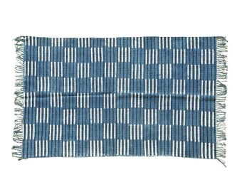 May include: A rectangular blue and white patterned throw blanket. The blanket features a grid design of vertical white stripes against a blue background. The edges have a fringe detail. This textile is suitable for home decor.