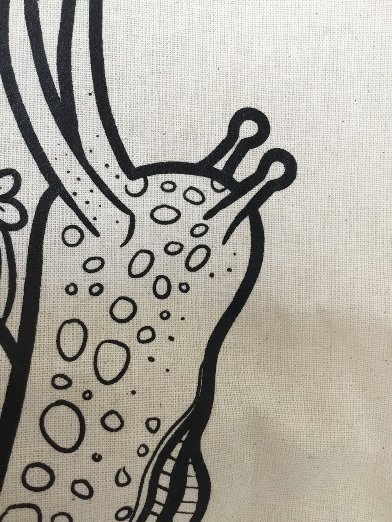 May include: Close-up of a canvas with a black, hand-drawn illustration of a stylized creature. The design features a rounded body with numerous oval-shaped spots and two antennae-like structures.