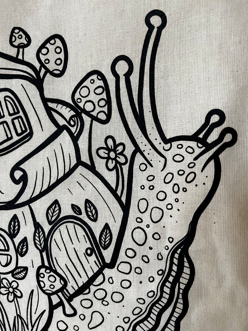 May include: Black and white illustration of a snail carrying a house on its back. The snail's shell is decorated with a whimsical house, mushrooms, and flowers. The design is on a beige fabric.
