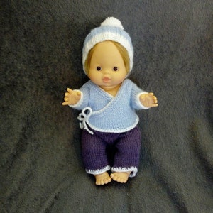 Könnte beinhalten: Eine gestrickte Puppe mit einer blau-weiß gestreiften Mütze, einem hellblauen Pullover mit weißem Rand und einer lila Hose mit weißem Rand.
