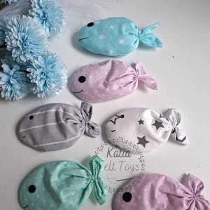 May include: A collection of handmade fabric fish toys in various pastel colors, including blue, pink, gray, and mint green. Each fish features a stitched face and a knotted tail. Some are patterned with stars or stripes.