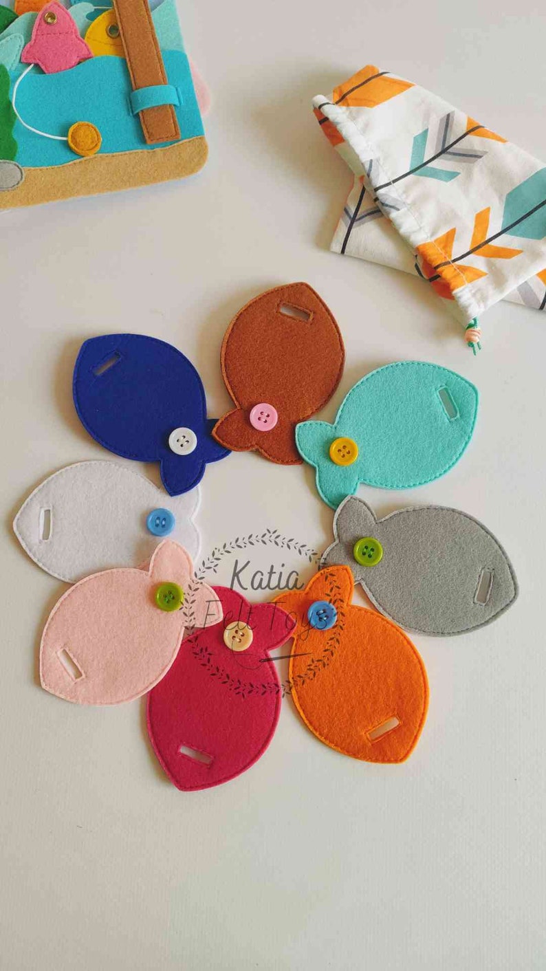 May include: A set of eight felt fish with different colors and buttons. The fish are arranged in a circle on a white surface.