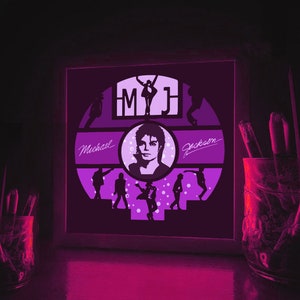 K&ouml;nnte beinhalten: Ein gerahmtes beleuchtetes Kunstwerk mit einer Silhouette von Michael Jackson mit dem Text "MJ" und "Michael Jackson" in einem lila und wei&szlig;en Farbschema.