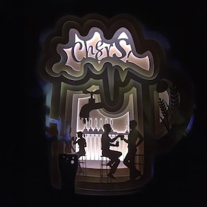 May include: A paper cut-out design of a bar with a tap and three people drinking. The bar is lit from behind and the word "Cheers!" is cut out above the bar.