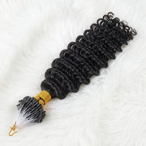 May include: A bundle of black, curly hair extensions. The hair is tightly curled and appears to be synthetic. The base of the extensions is wrapped in gold thread and features small, black beads and a metal hook.