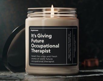 May include: A beige candle in a glass jar with a black label that reads "It's Giving Future Occupational Therapist". The candle is lit and the label also includes the text "Smell the crisp and fresh aroma of 100% future occupational therapist".