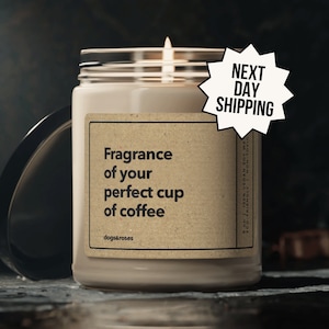 May include: A brown candle with a white label that reads "Fragrance of your perfect cup of coffee" and "dogs&roses". The candle is lit and has a white flame. The candle is on a dark surface. The text "NEXT DAY SHIPPING" is in a white speech bubble.