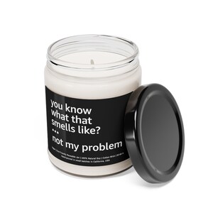 Puede incluir: Una vela blanca en un frasco de vidrio transparente con una tapa negra. La vela tiene una etiqueta negra con texto blanco que dice "you know what that smells like? ... not my problem."