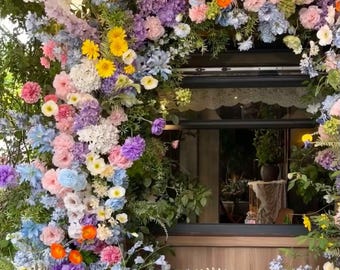 May include: A floral archway made of various flowers in shades of pink, purple, blue, yellow, and white. The flowers are arranged in a cascading design, creating a beautiful and romantic backdrop.